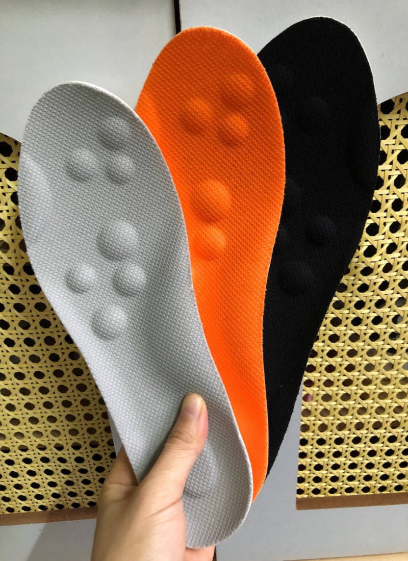 Three shoe insoles in gray, orange, and black held by a hand on a textured surface.